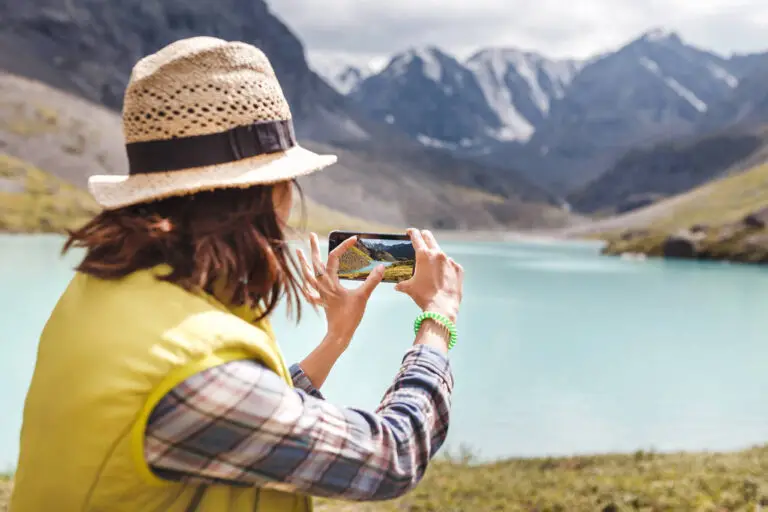 woman hiker taking photo of a mountain lake on her smartphone