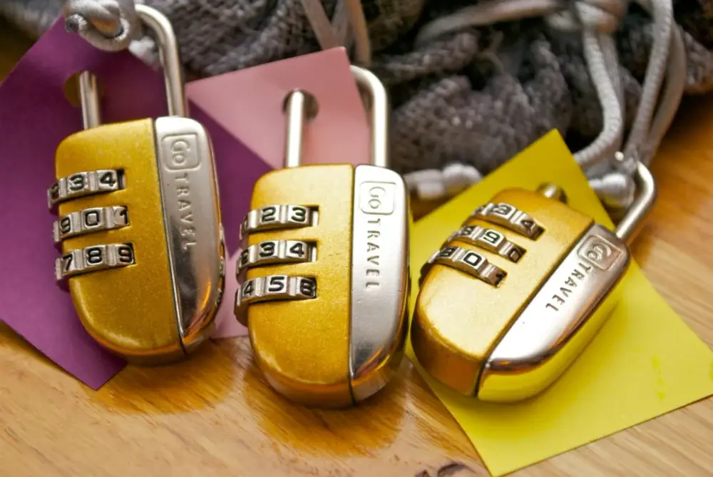 Three gold combination padlocks branded "TRAVEL" rest on colored paper squares, symbolizing security. Essential solo travel safety items for secure journeys.