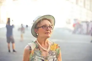 Elderly woman in a hat and floral dress gazes thoughtfully, set against a blurred street background. A serene moment in one of the best vacation destinations for single seniors