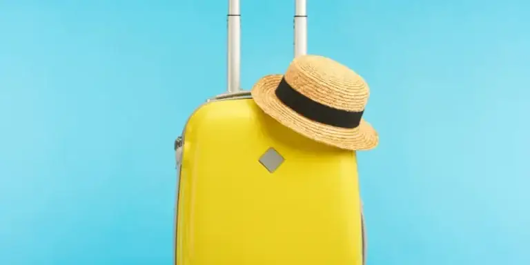 Bright yellow suitcase with an extended handle and a straw hat on top against a blue background, symbolizing adventure. Best luggage for solo travelers seeking convenience.