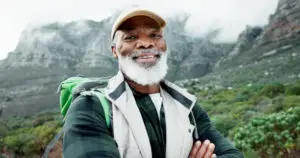 Confident senior Black man hiking in nature, smiling while exploring scenic trails. A great example of adventure in the best travel destinations for single seniors.