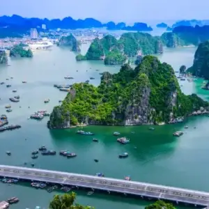 Halong Bay one of best cities in vietnam to visit, featuring lush green islands surrounded by turquoise water. Boats dot the bay, and a bridge crosses the foreground.