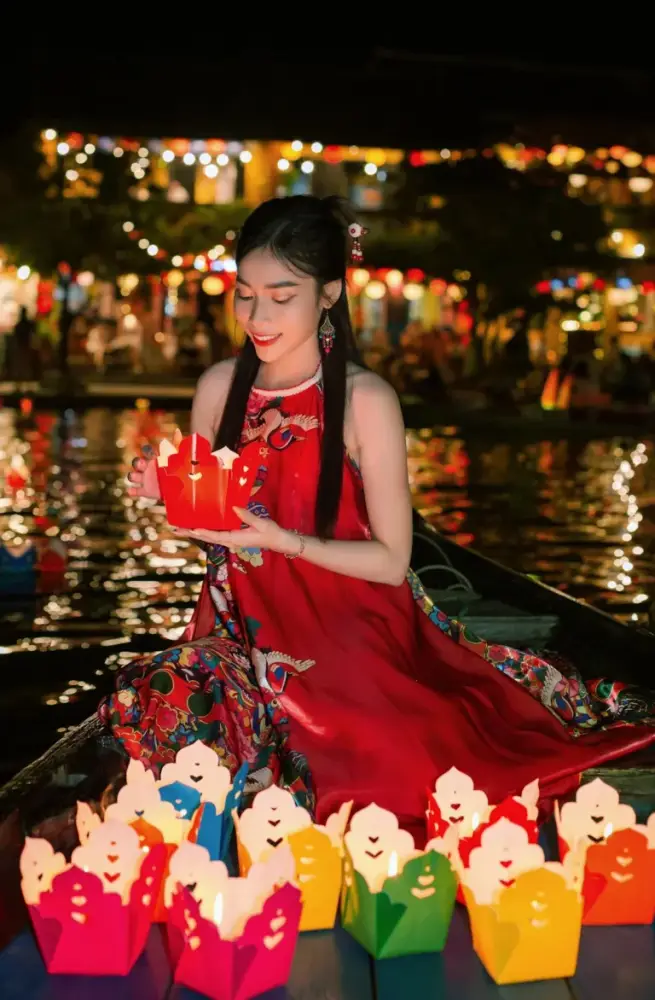 A woman in a red dress sits on a boat, smiling at a glowing lantern during Vietnam’s lantern festival. Festive nighttime scene highlights the best time to visit Vietnam.