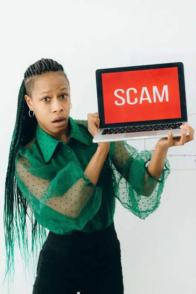 Concerned person in a green blouse holding a laptop with "SCAM" in bold red text, highlighting travel safety concerns. Is Vietnam a safe country to travel?